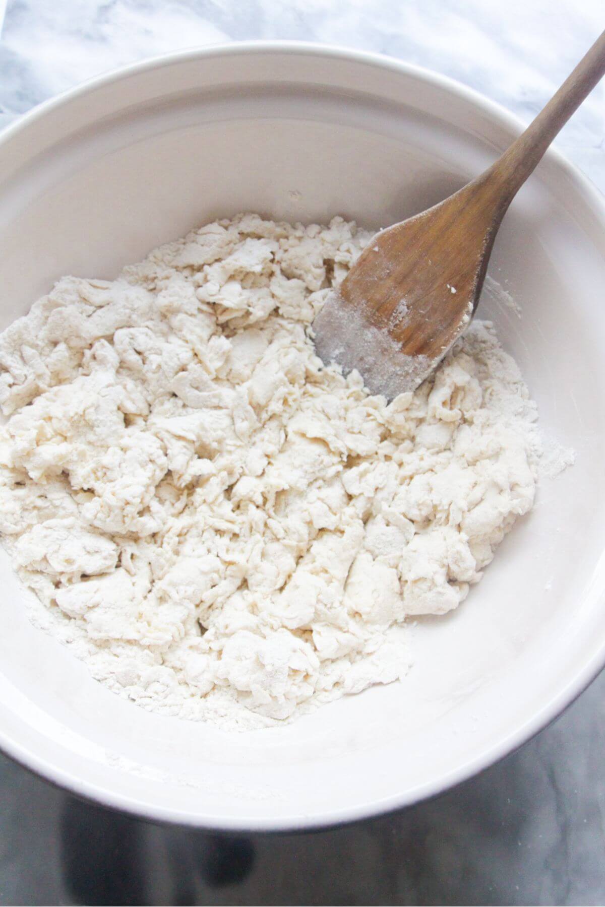 Wooden spatula in a large white bowl with crumbly yogurt and flour mixture.