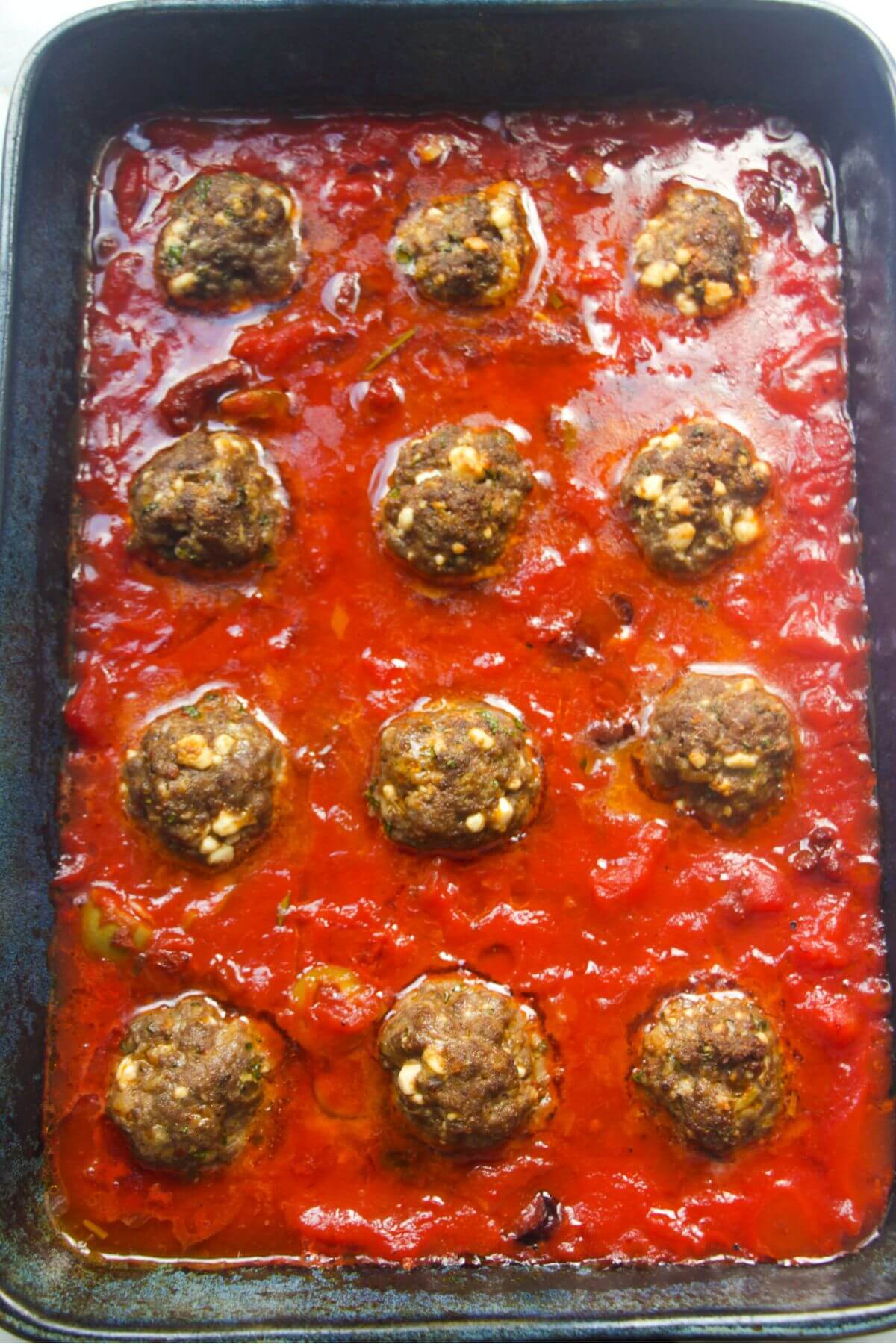 12 par-cooked meatballs in tomato sauce in a large blue oven dish.