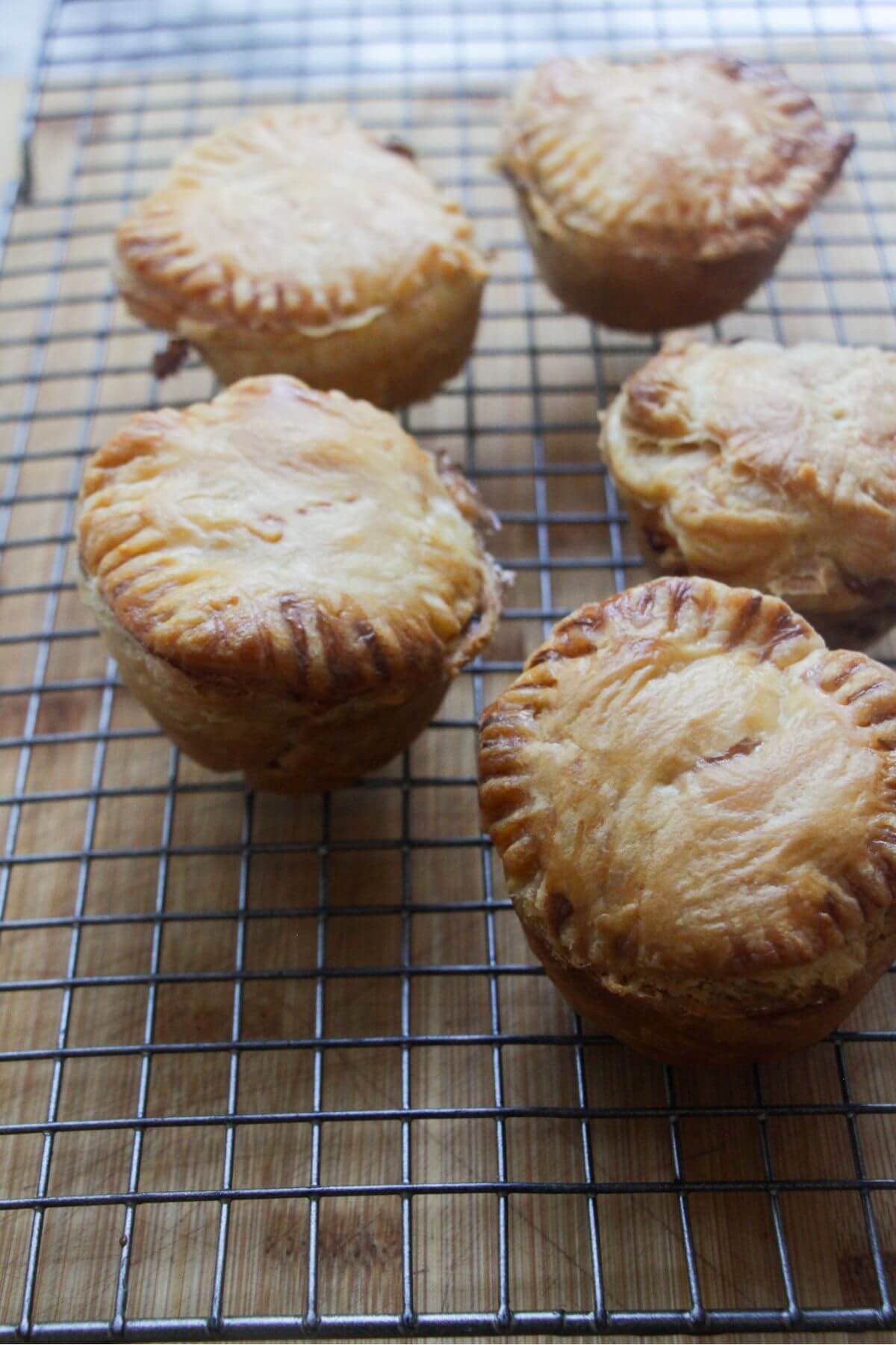 Close up of 5 cooked mince and cheese pies sitting on a silver wire rack.