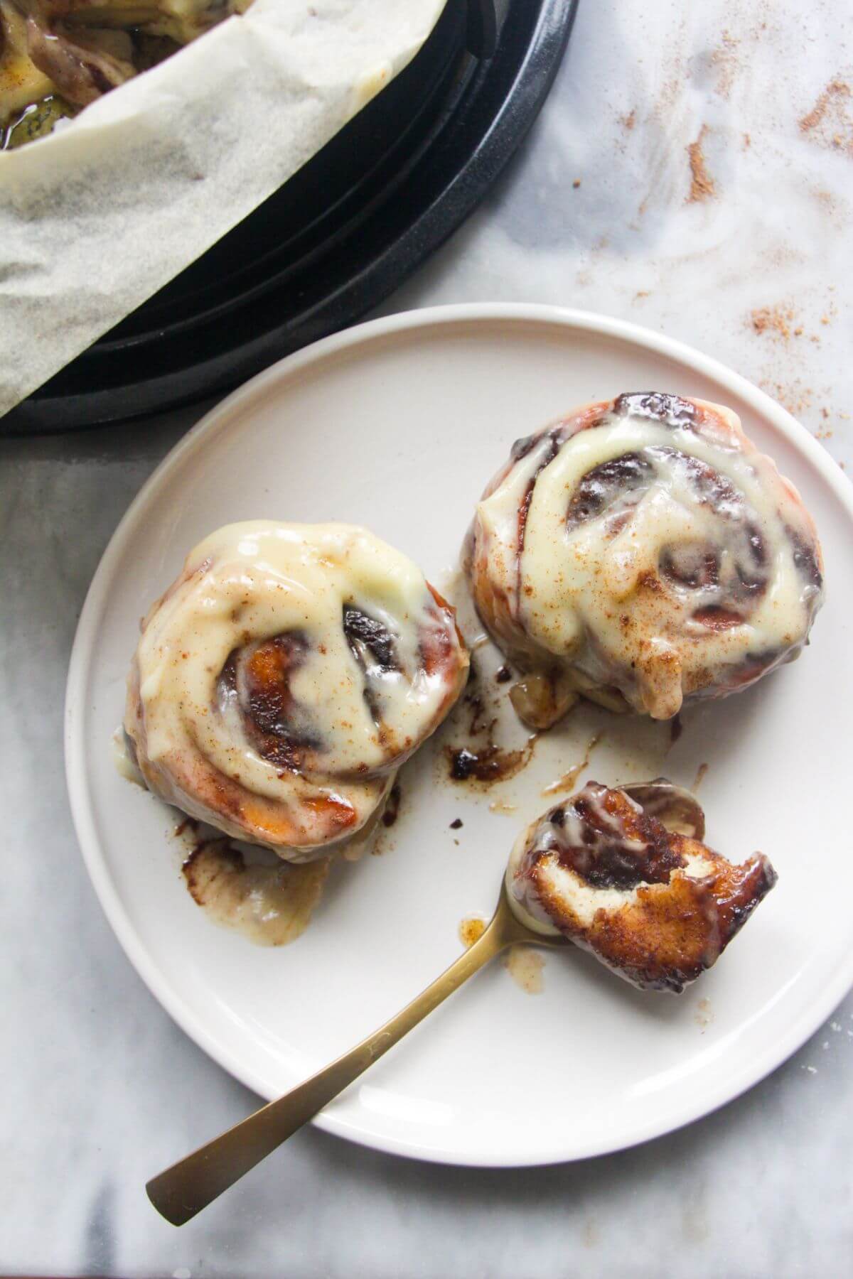 Close up of 2 pumpkin spice cinnamon rolls on a white plate with a small spoon.