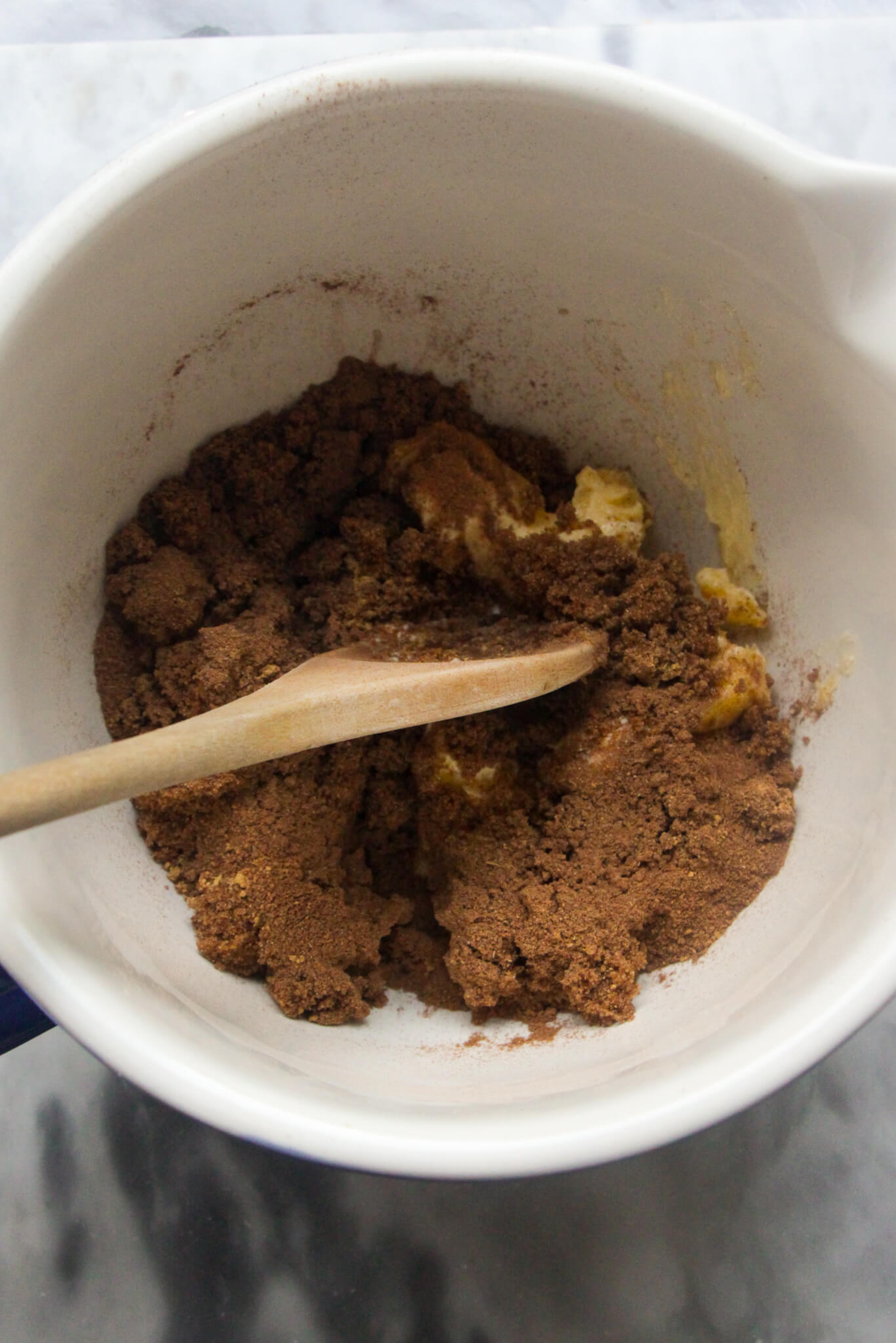 Pumpkin spice, butter and brown sugar in a white mixing bowl with a wooden spoon starting to mix it into a paste.