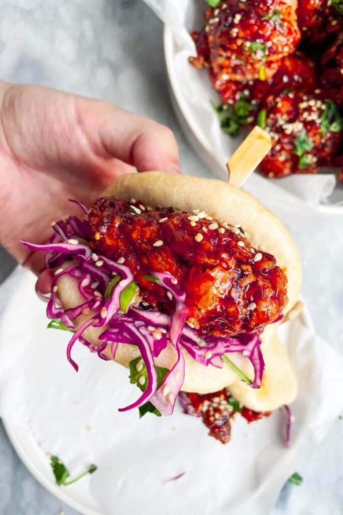 Hand holding up a bao bun filled with Korean fried chicken and red cabbage slaw.