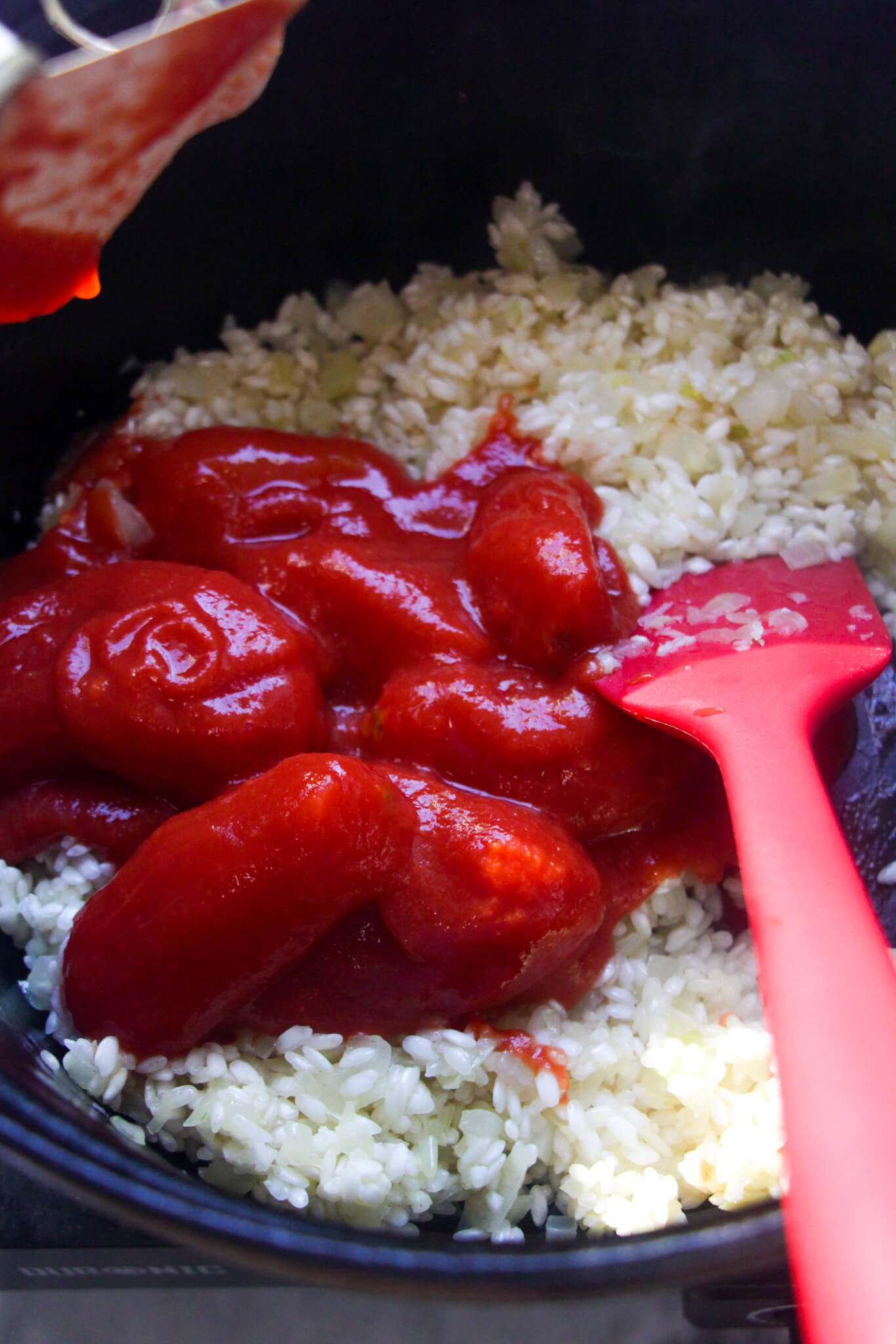 Tinned plum tomatoes added to rice, onions and garlic in a black pot.