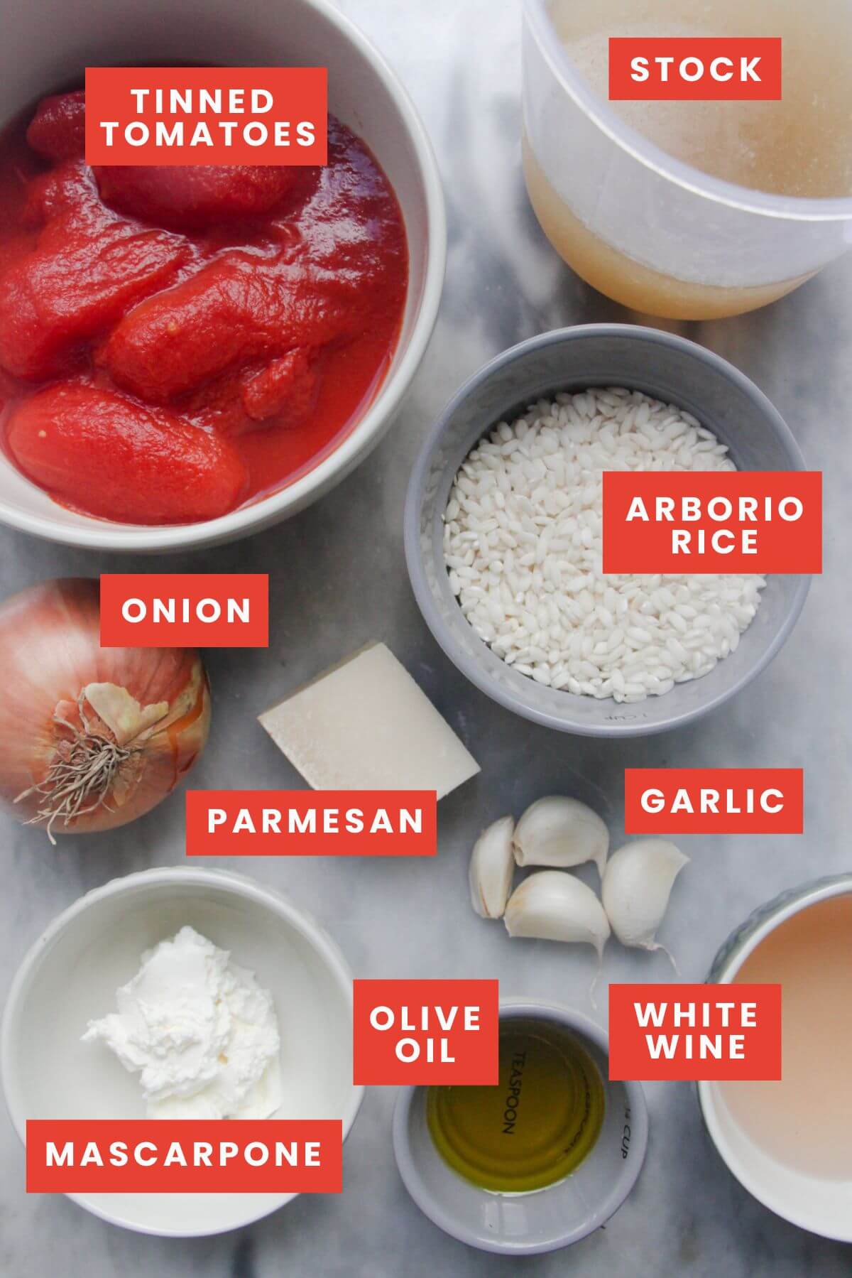 Ingredients for tomato mascarpone risotto laid out on a marble background and labelled.
