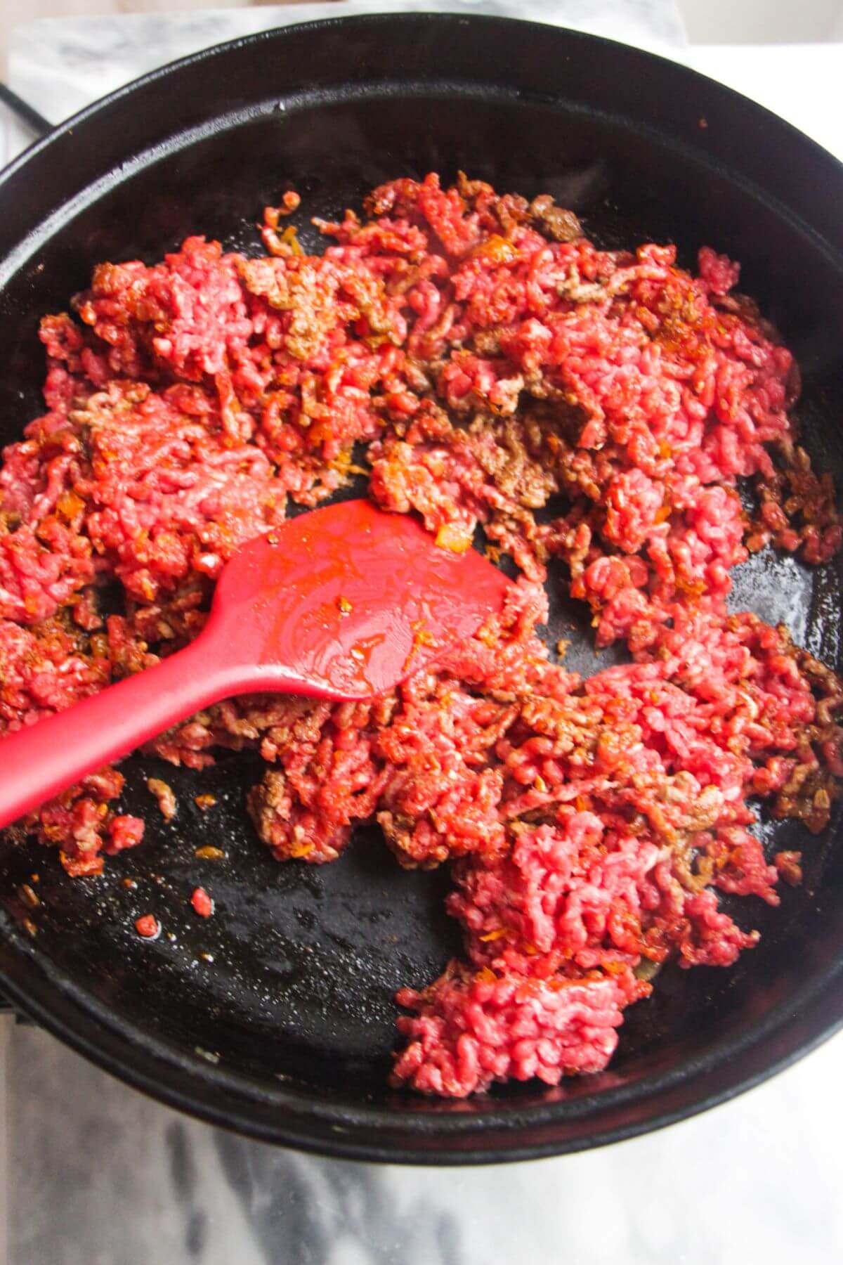 Beef mince added to a large black pan with a red spatula stirring it.