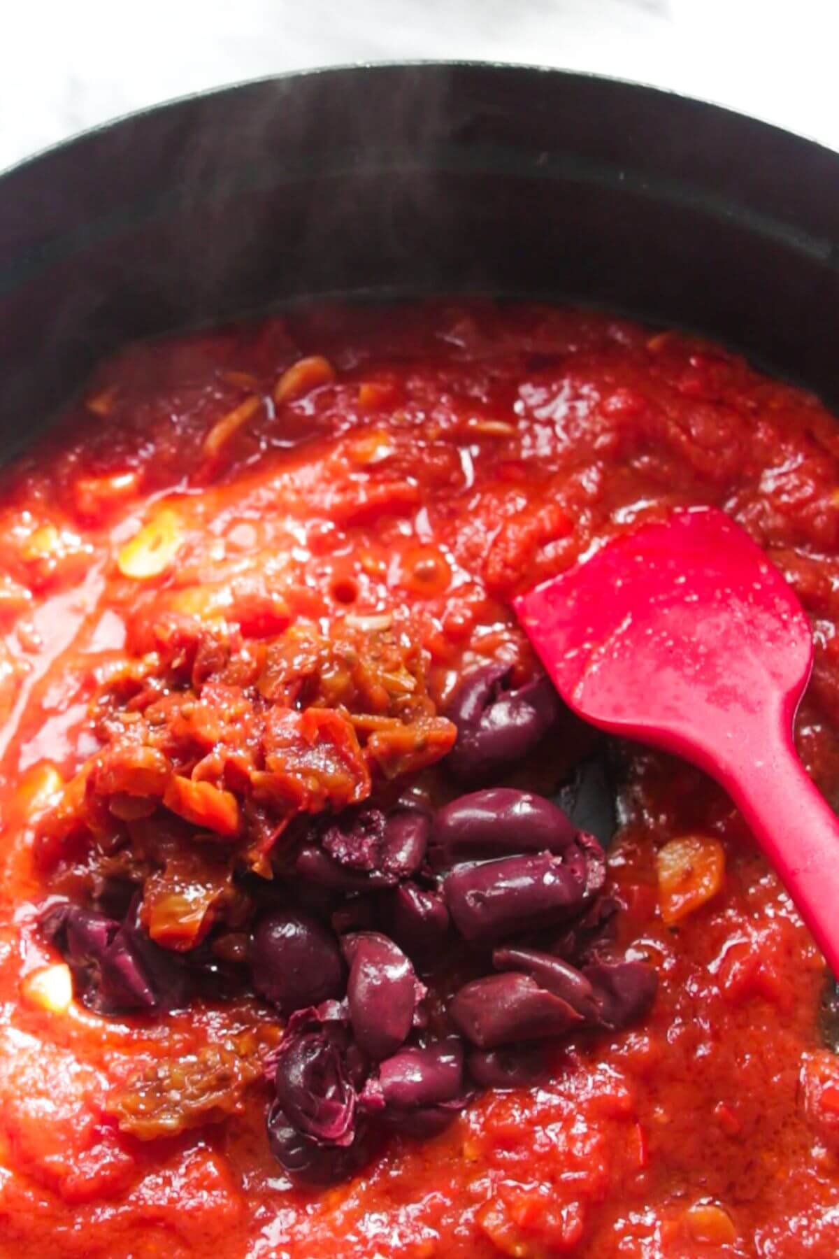 Kalamata olives and sundried tomatoes in a tomato sauce in a large black skillet.
