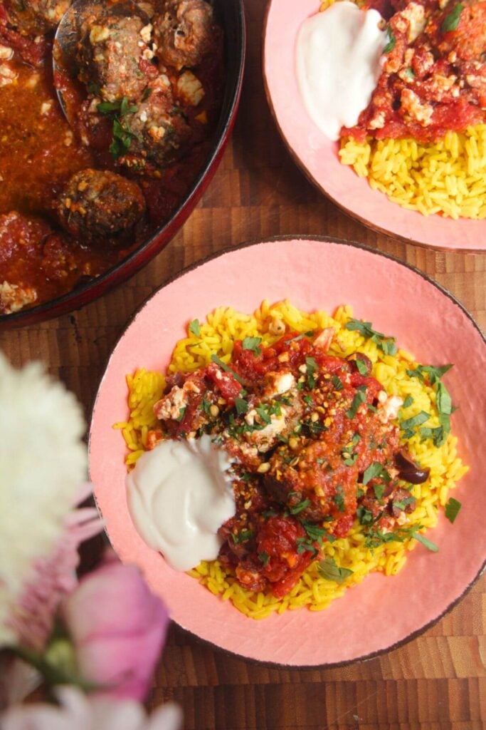 Baked meatballs in tomato sauce on top of golden rice in a pink bowl.