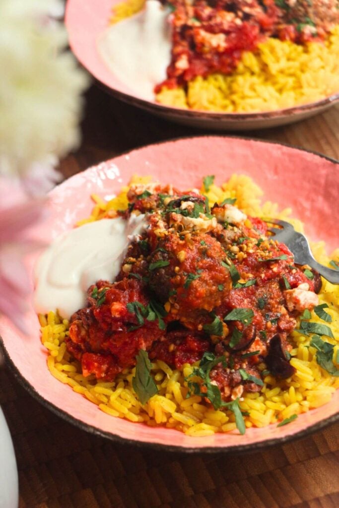 Baked meatballs in tomato sauce on top of golden rice in a pink bowl.
