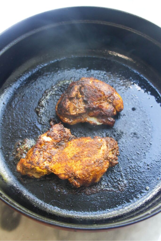 Cooked chicken thighs in a large black skillet.