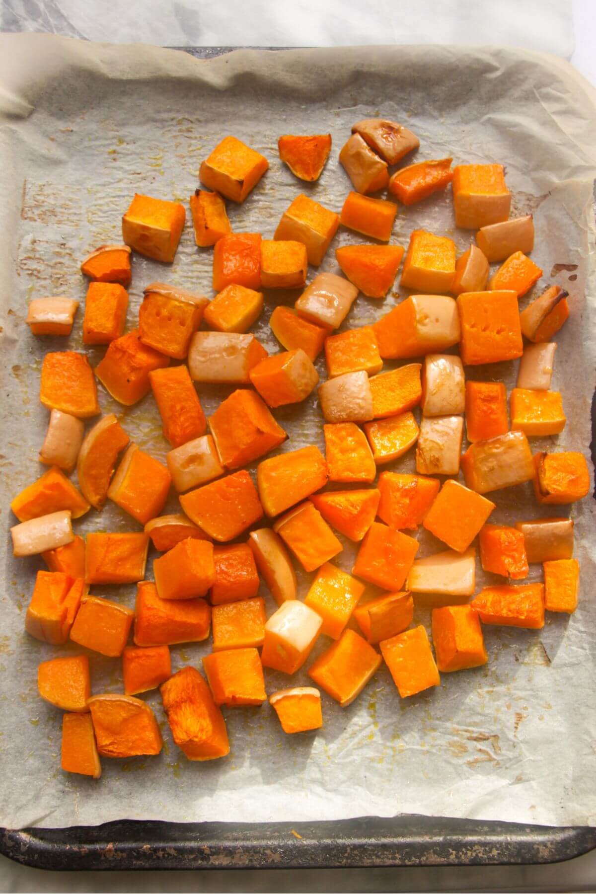Cooked butternut squash cubes on a lined oven tray.
