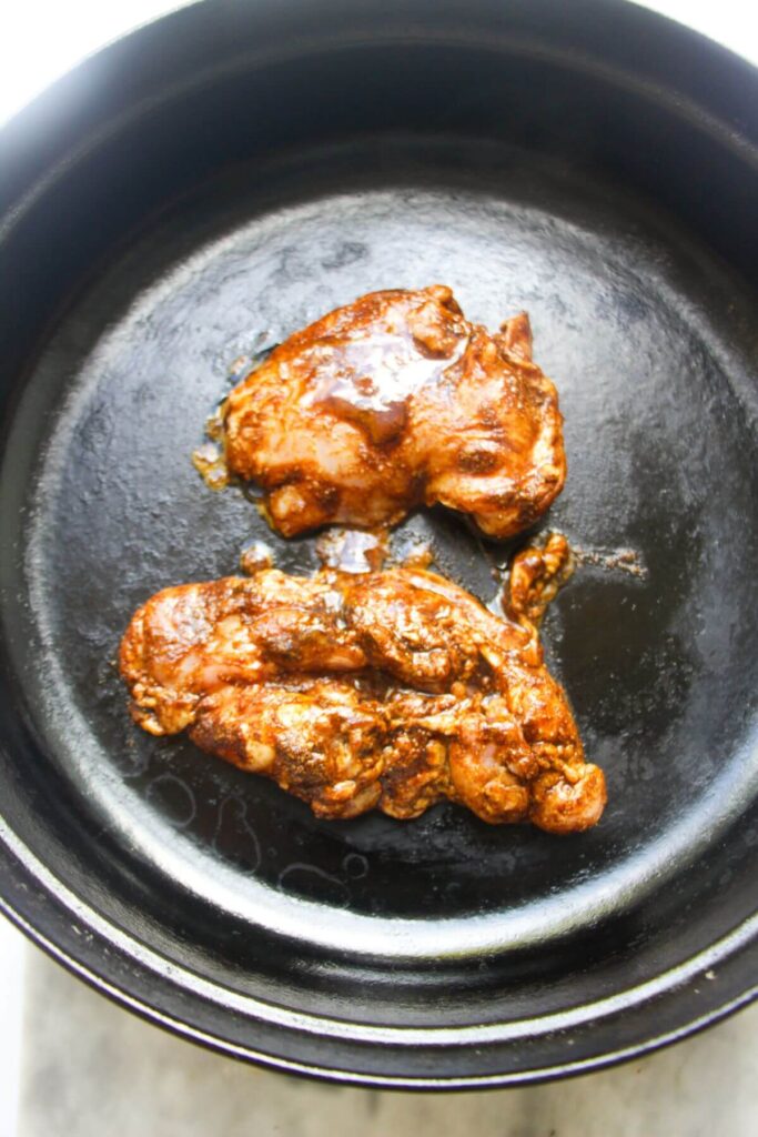 Marinated chicken thighs in a large black skillet.