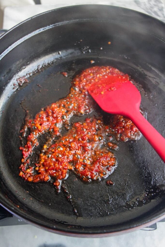 Red spatula stirring 'nduja paste in a large black skillet.