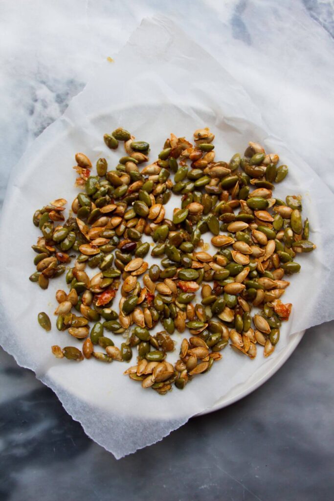 Sticky pumpkin seeds on a small baking paper lined plate.