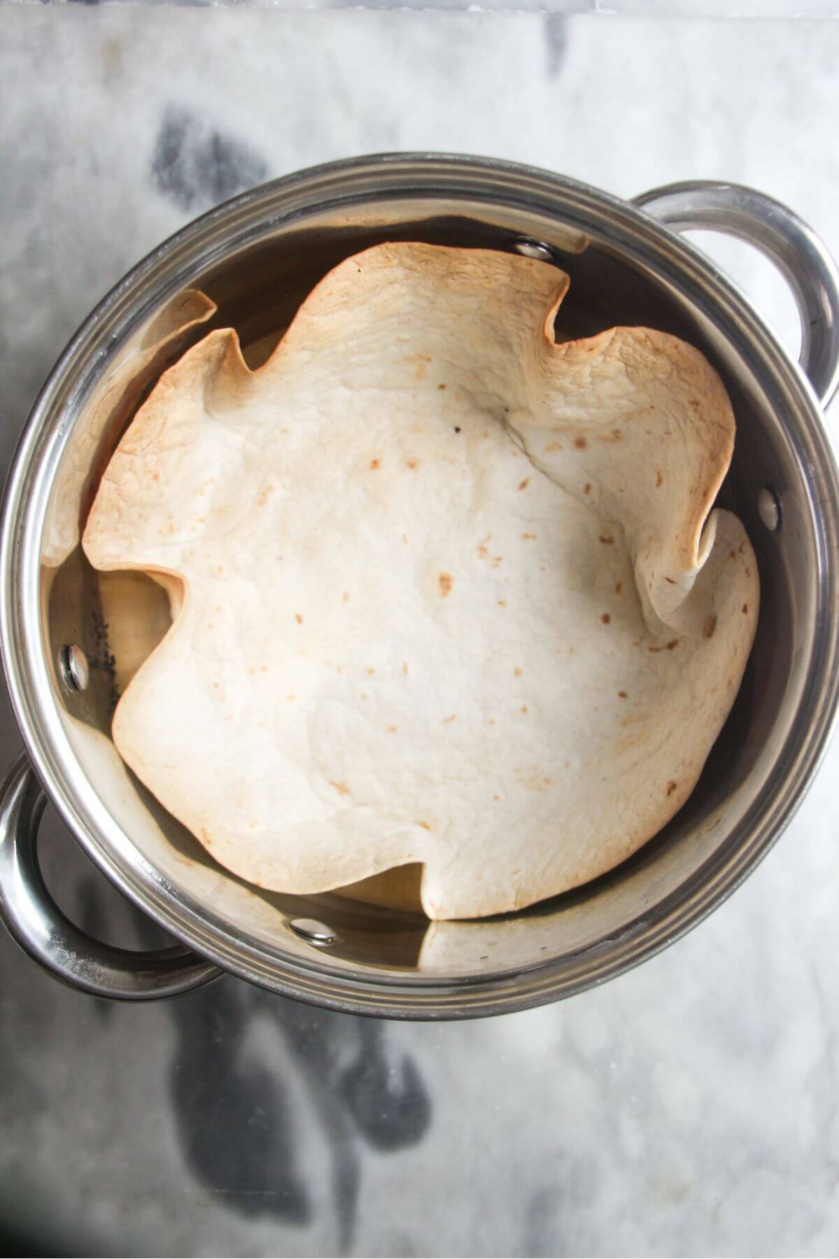 Crispy tortilla shell in a small silver pot on a grey marble background.
