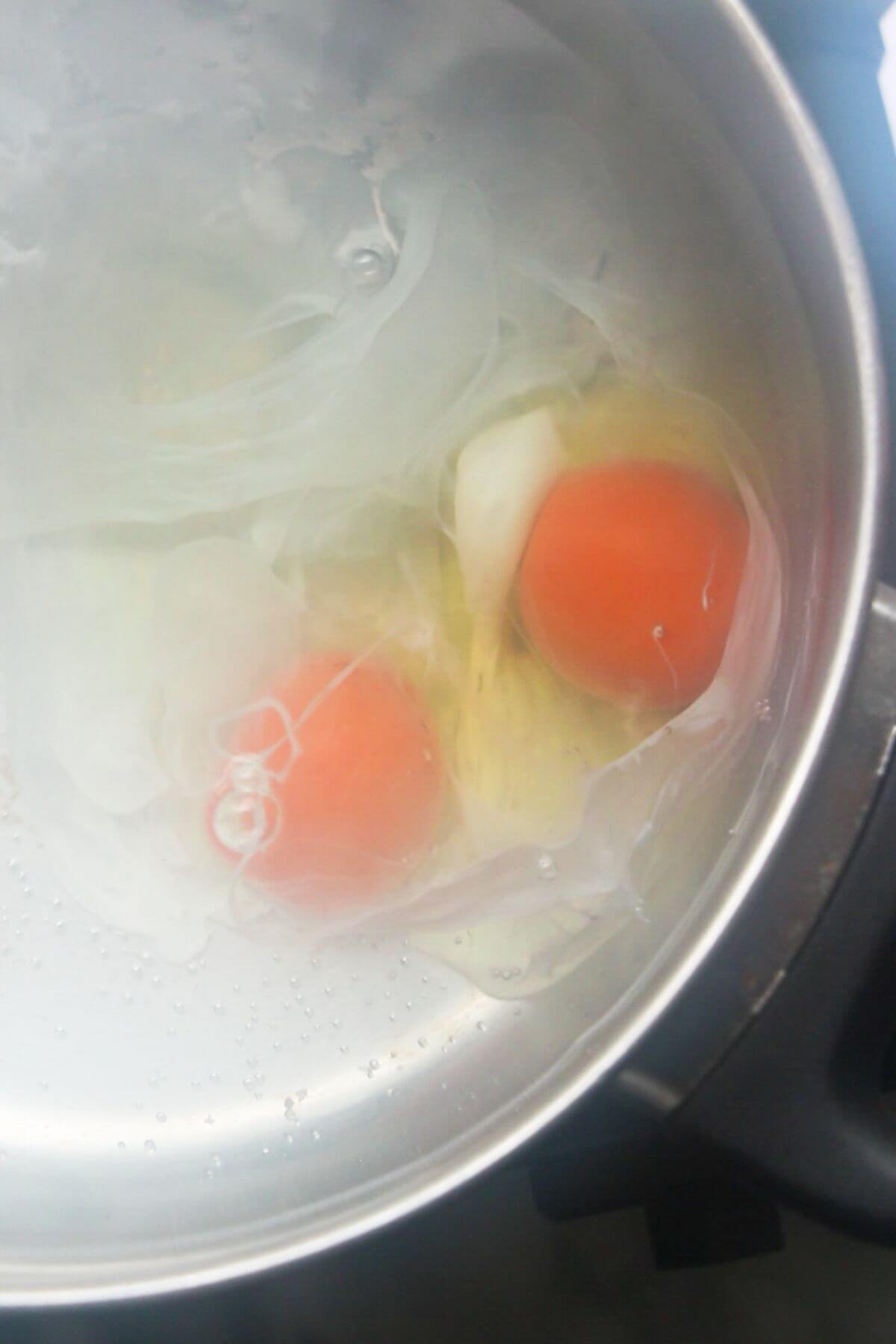 Close up of 2 eggs in water in a silver pan, starting to be poached.