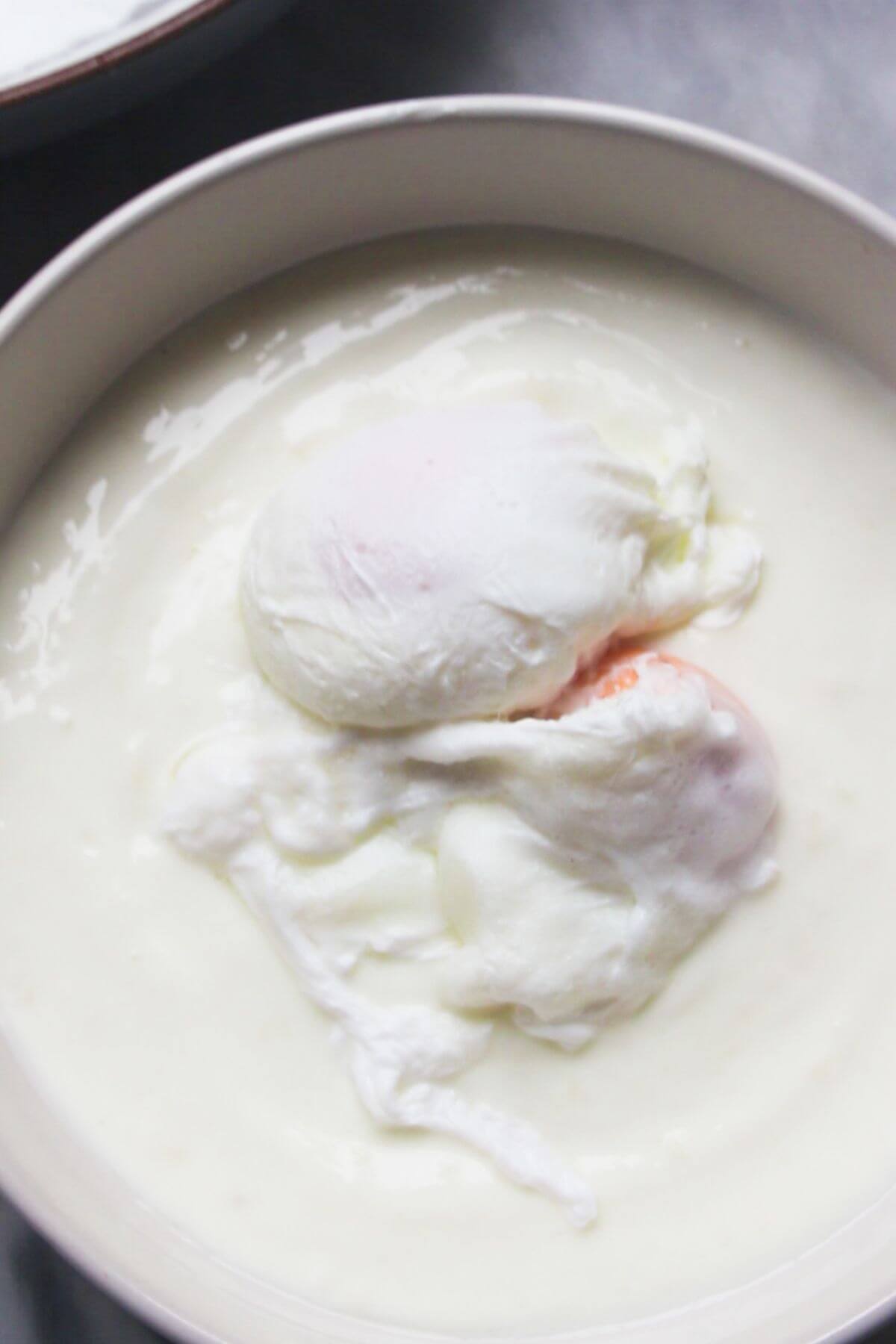 2 poached eggs sitting on top of garlicky yogurt in a small white bowl.