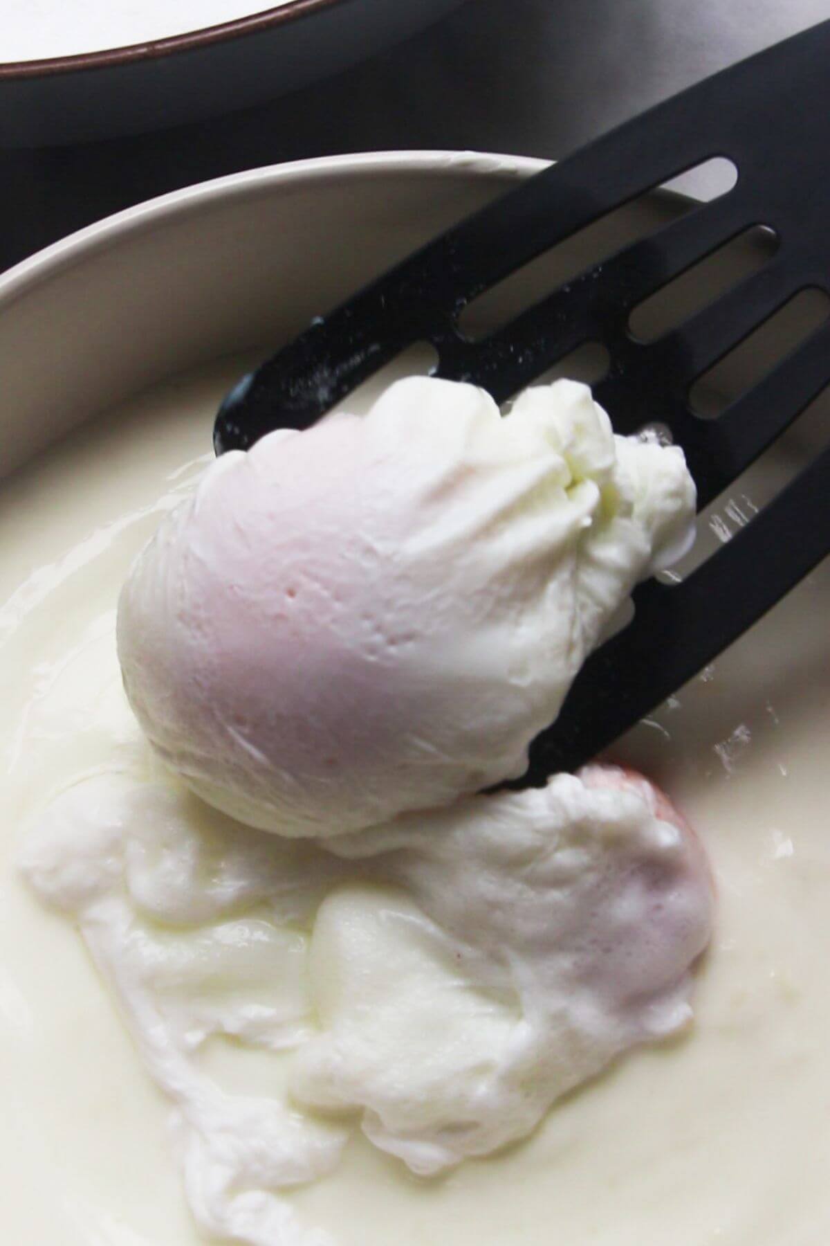 Black spatula transferring a poached egg into a bowl with garlicky yogurt.