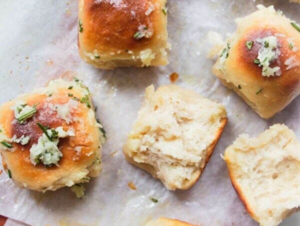 8 garlic butter topped rolled assembled on a baking paper lined wooden board with bowl of garlic butter in the background and one roll torn open.