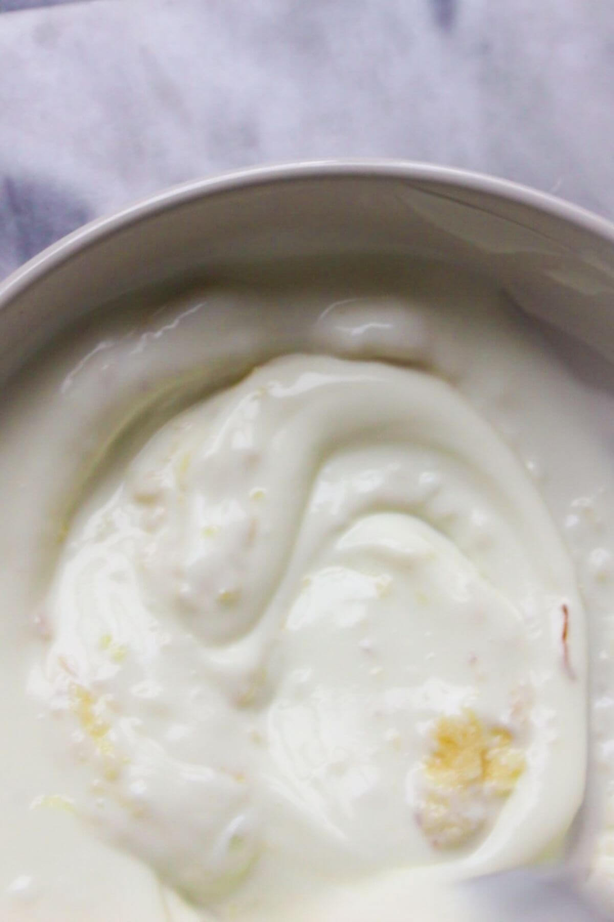 Yogurt and crushed garlic in a small white bowl on a grey marble background.
