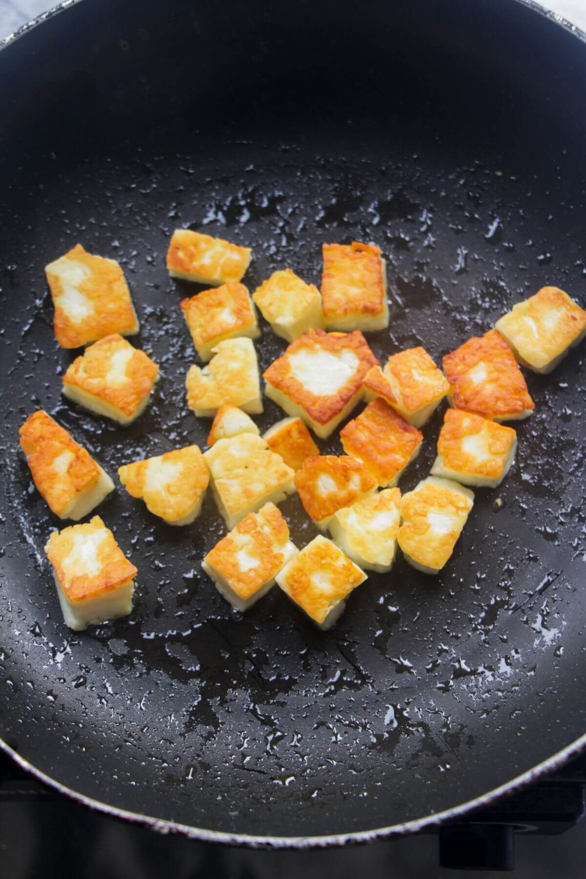 Golden halloumi croutons in a small black pan.