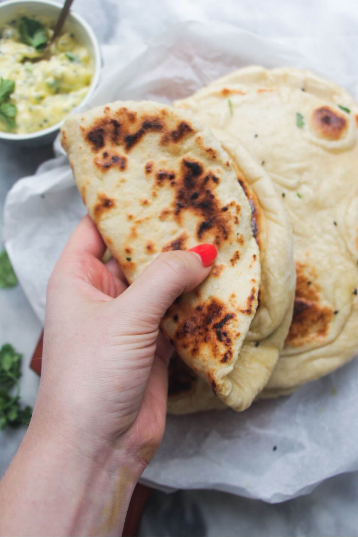 A hand handing a folded piece of garlic naan, with a pile of naan in the background.