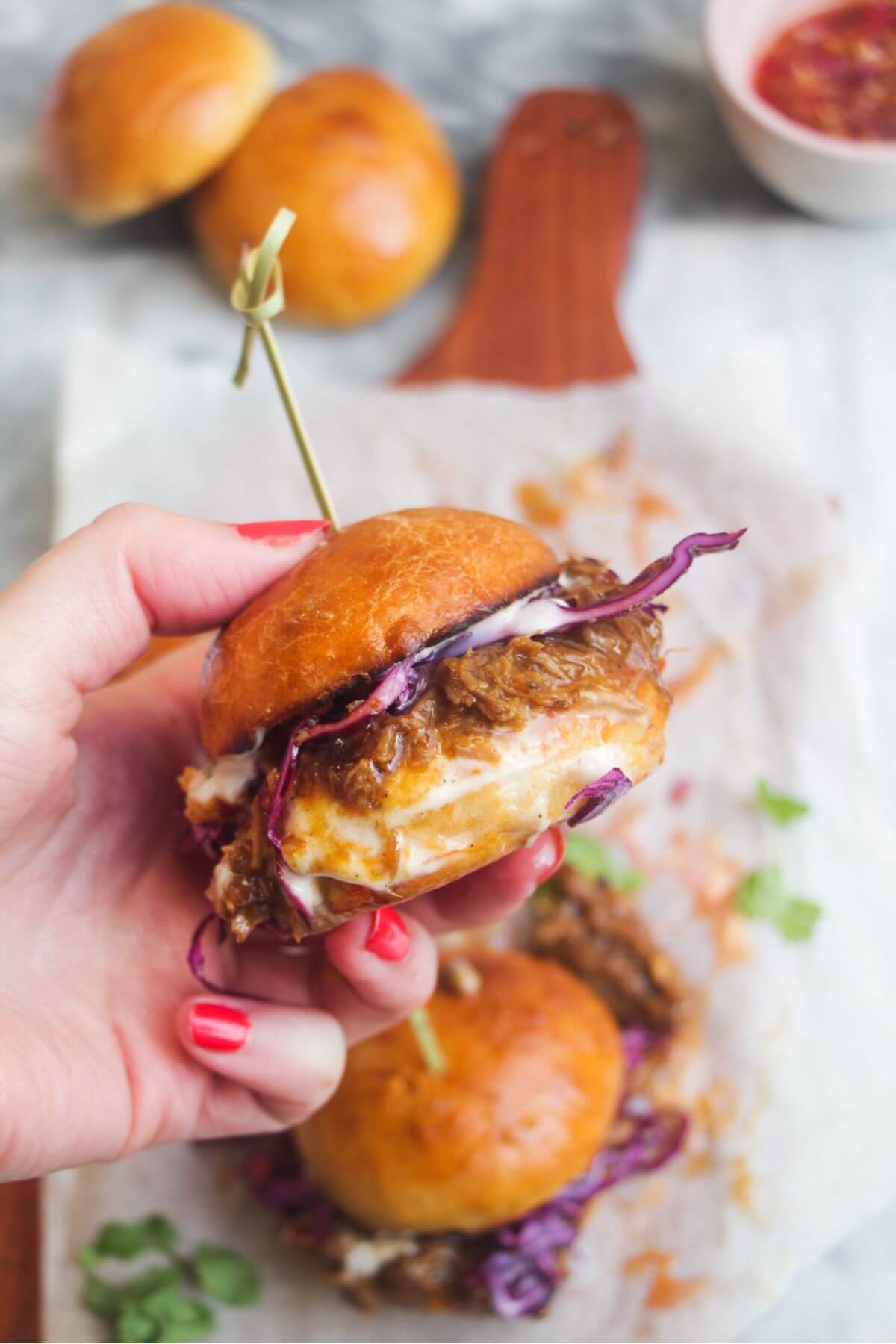 Hand holding up a pulled pork slider with more sliders in the background.