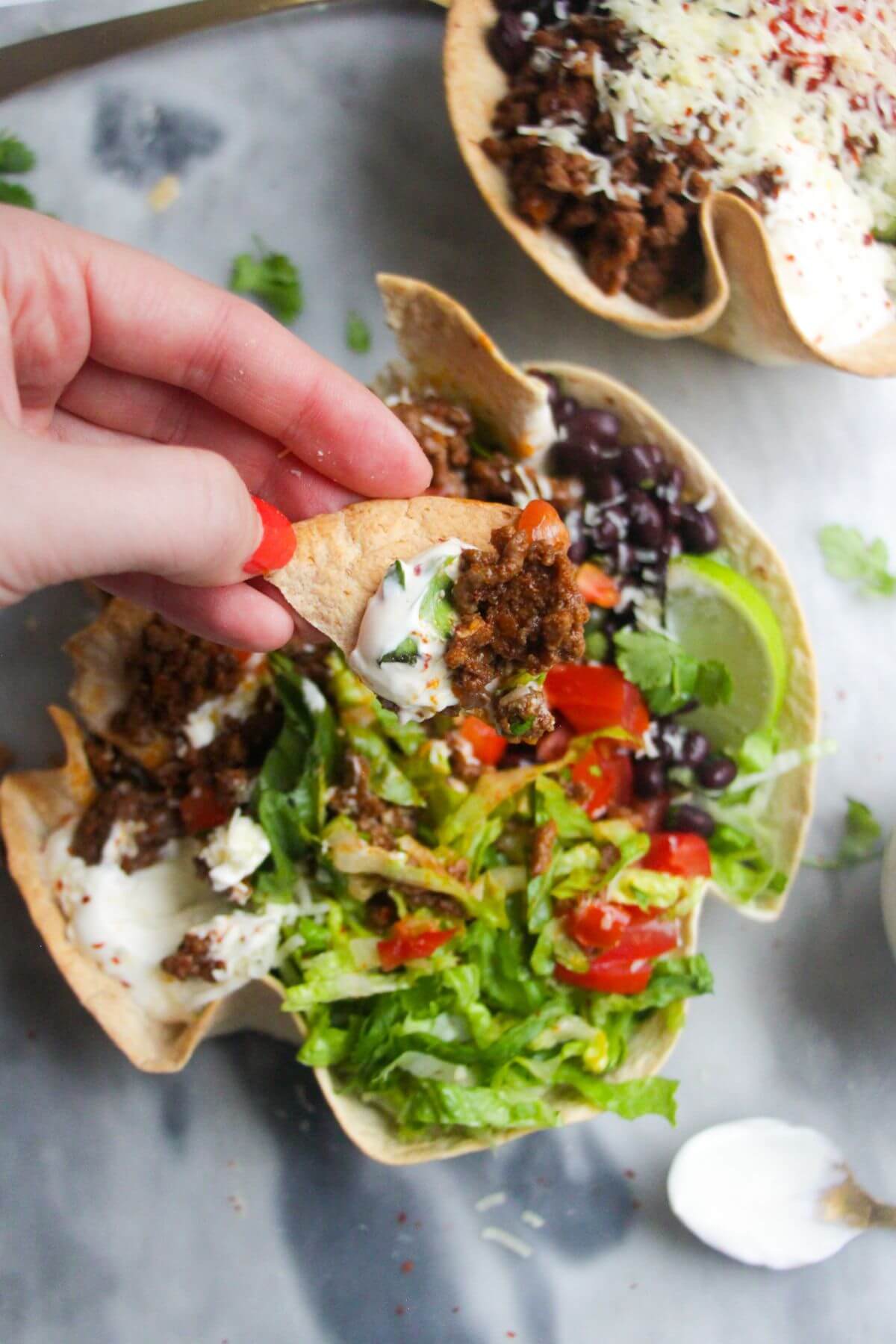 Hand holding a piece of crispy taco bowl with taco bowl ingredients on it.