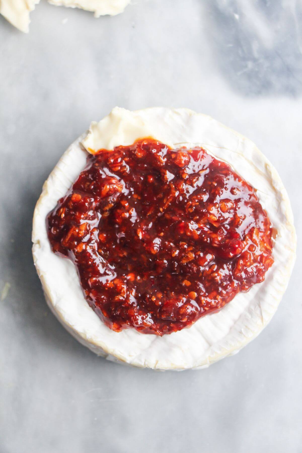 Honey and harissa sauce piled on top of small round of camembert on a grey marble background.