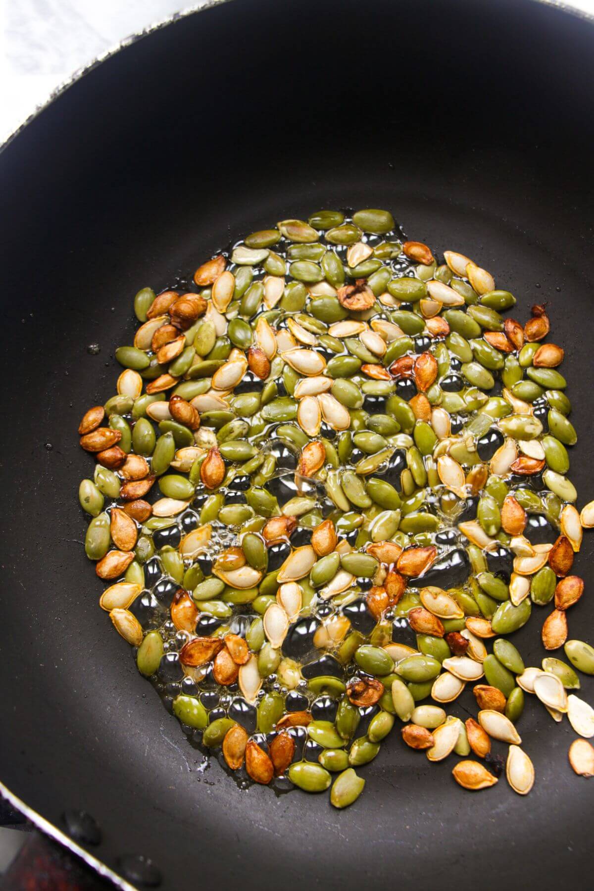Pumpkin seeds and honey cooking in a small black pan.