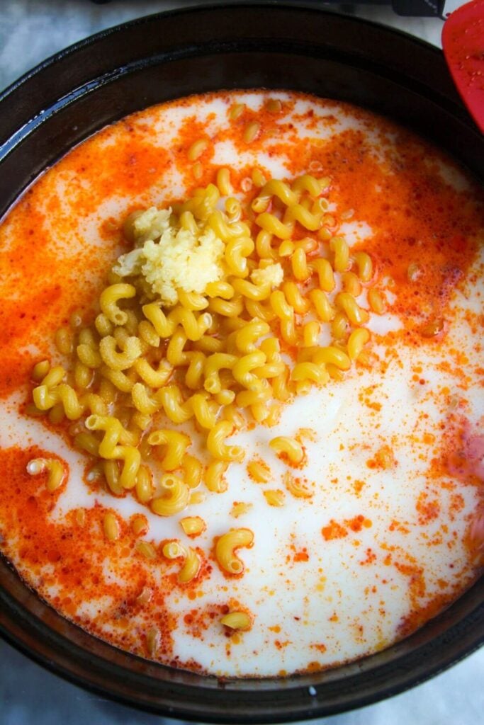 Milk, garlic and pasta added to 'nduja in a large black skillet.