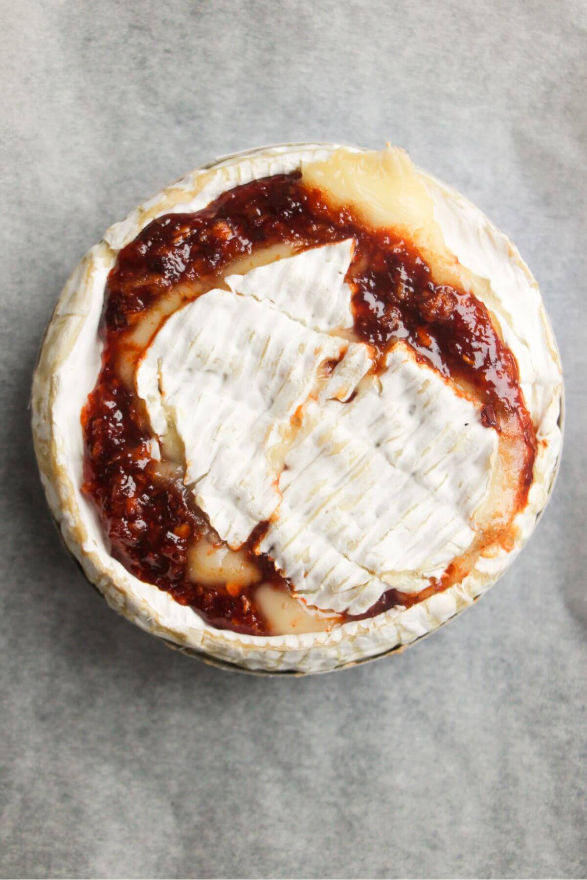 Camembert top placed over honey harissa sauce on a small wheel of camembert.