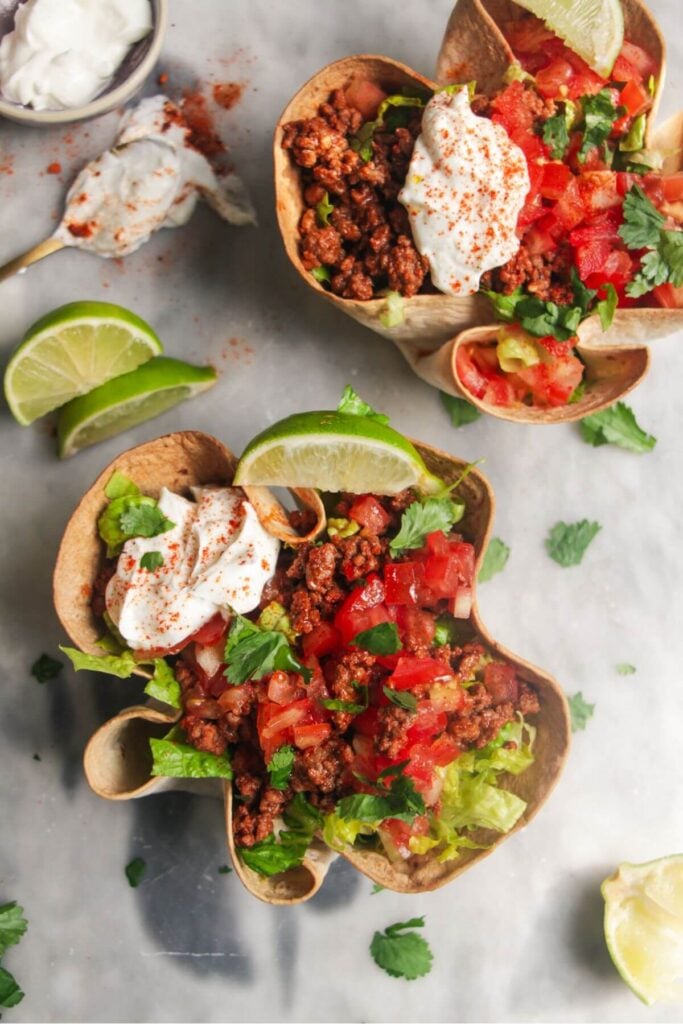 Two loaded burrito bowls on a grey background, with sour cream on the side and a lime wedge.