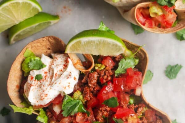 Two loaded burrito bowls on a grey background, with sour cream on the side and a lime wedge.