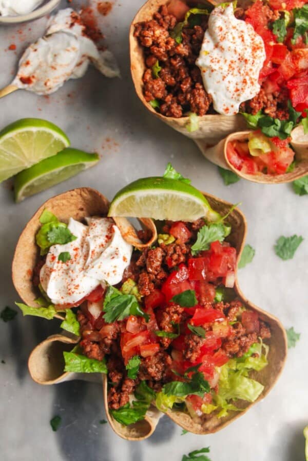 Two loaded burrito bowls on a grey background, with sour cream on the side and a lime wedge.