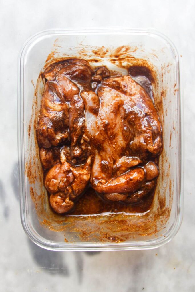 Chicken thighs marinating in shawarma spices in a small glass container.