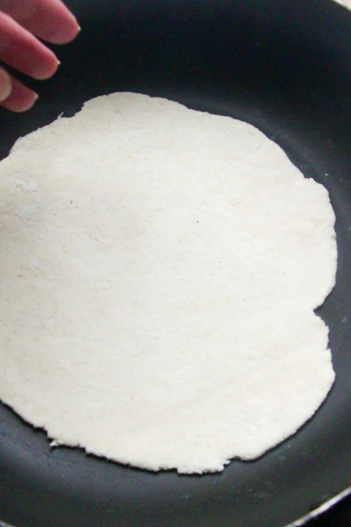 Rolled out naan being placed in a small black pan to cook.