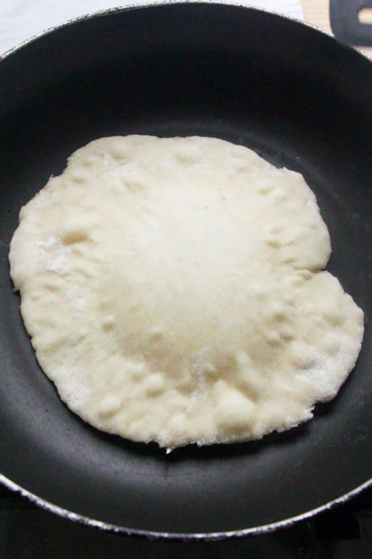 One naan in a small pan, puffing up as it cooks.
