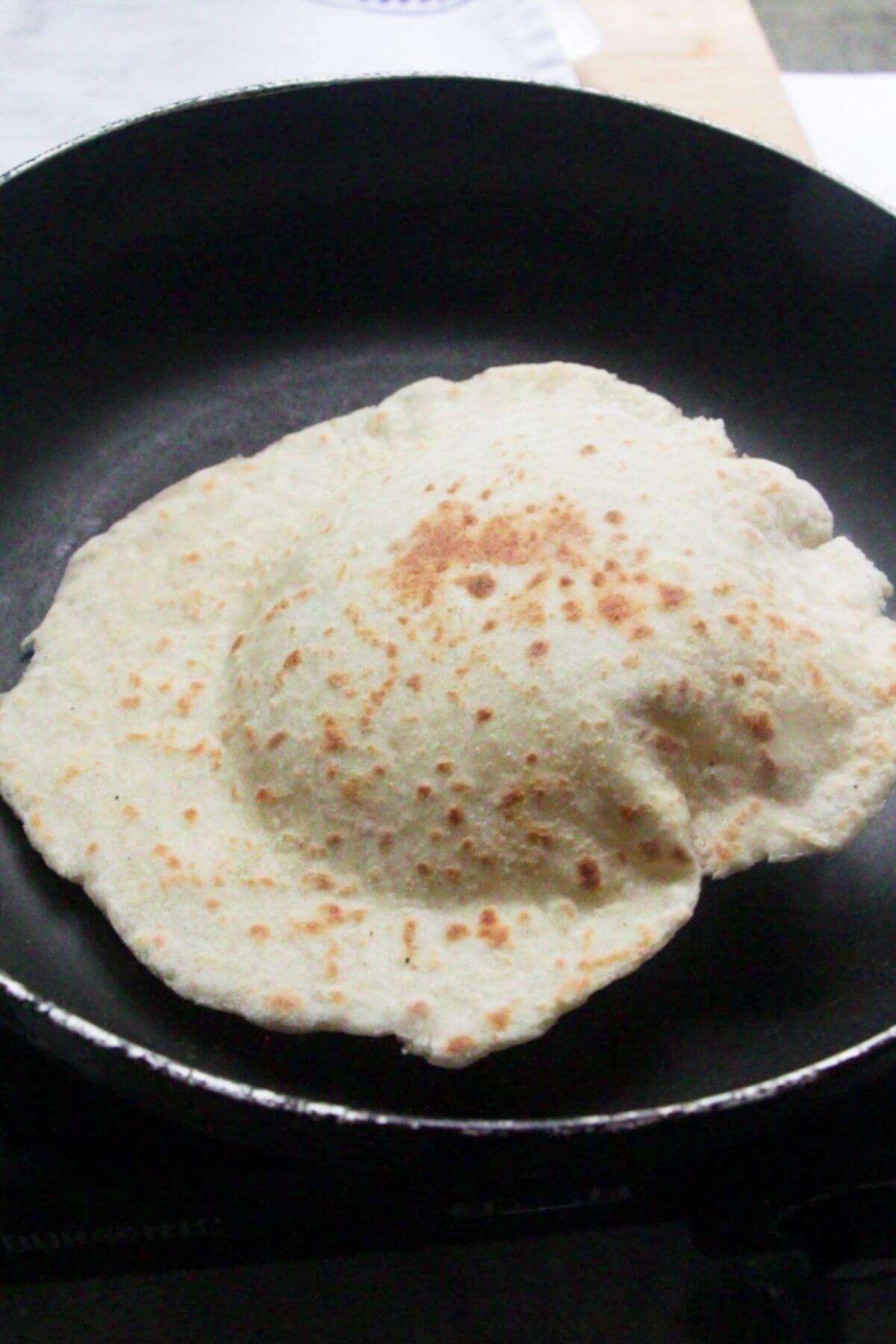 Naan in a small black pan, puffing up as it cooks.