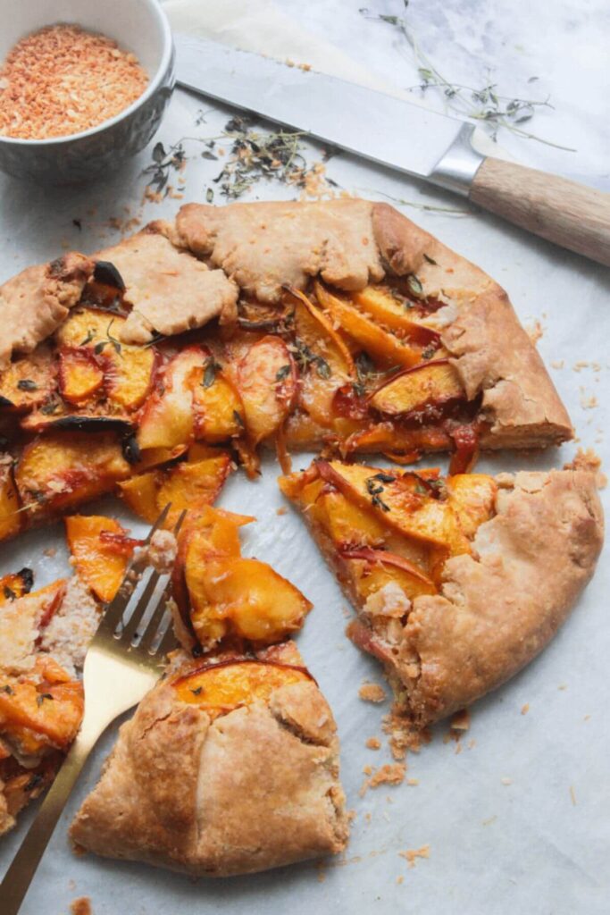 Sliced peach and almond galette on a grey background with a fork and knife in the background.