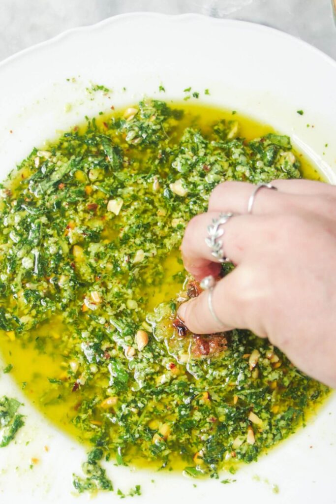 A hand sweeping bread through pesto dipping oil in a scalloped white plate.