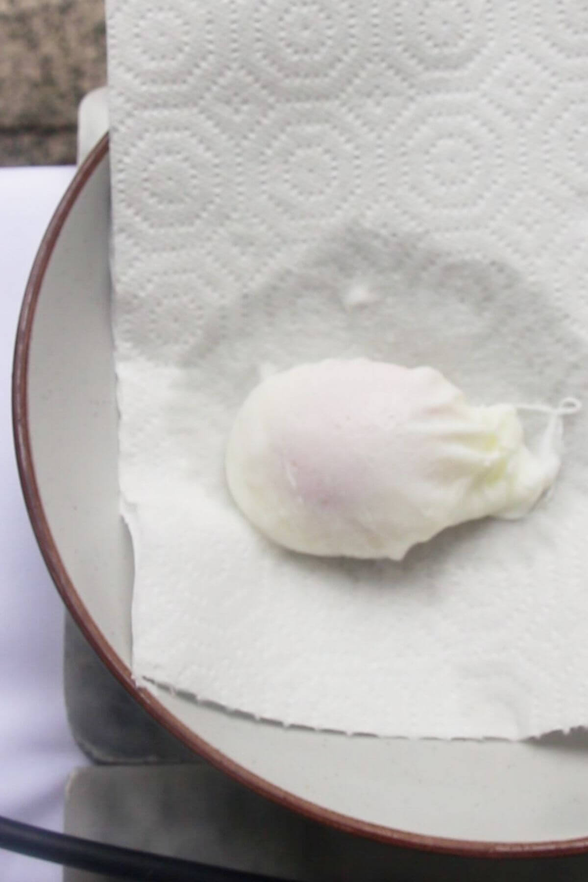 One poached egg draining on a paper towel on a plate.