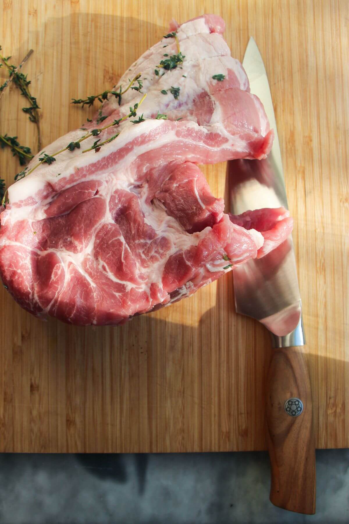 Piece of pork shoulder on a wooden board with a large knife next to it.