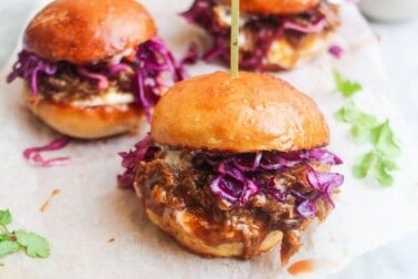 3 pulled pork sliders on a small wooden board.