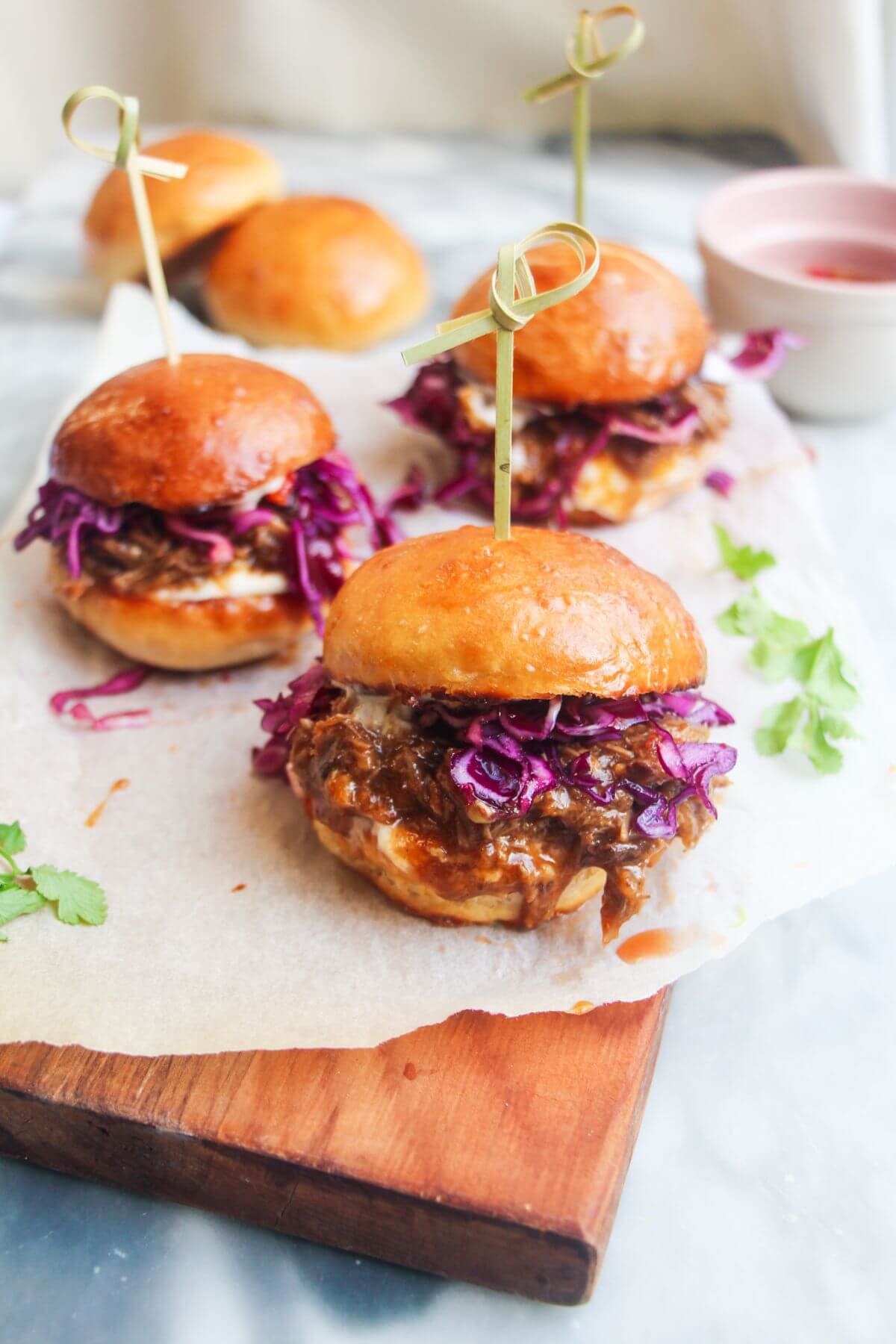 3 pulled pork sliders on a small wooden board.