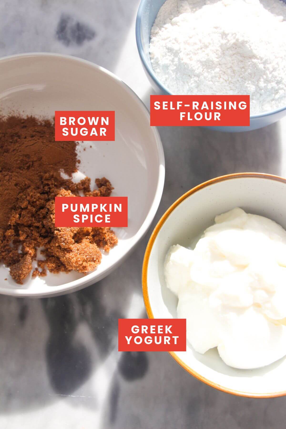 Ingredients for pumpkin spice donut bites laid out on a marble background and labelled.