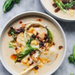 Roasted cauliflower cheese soup in 2 bowls on a grey marble background.