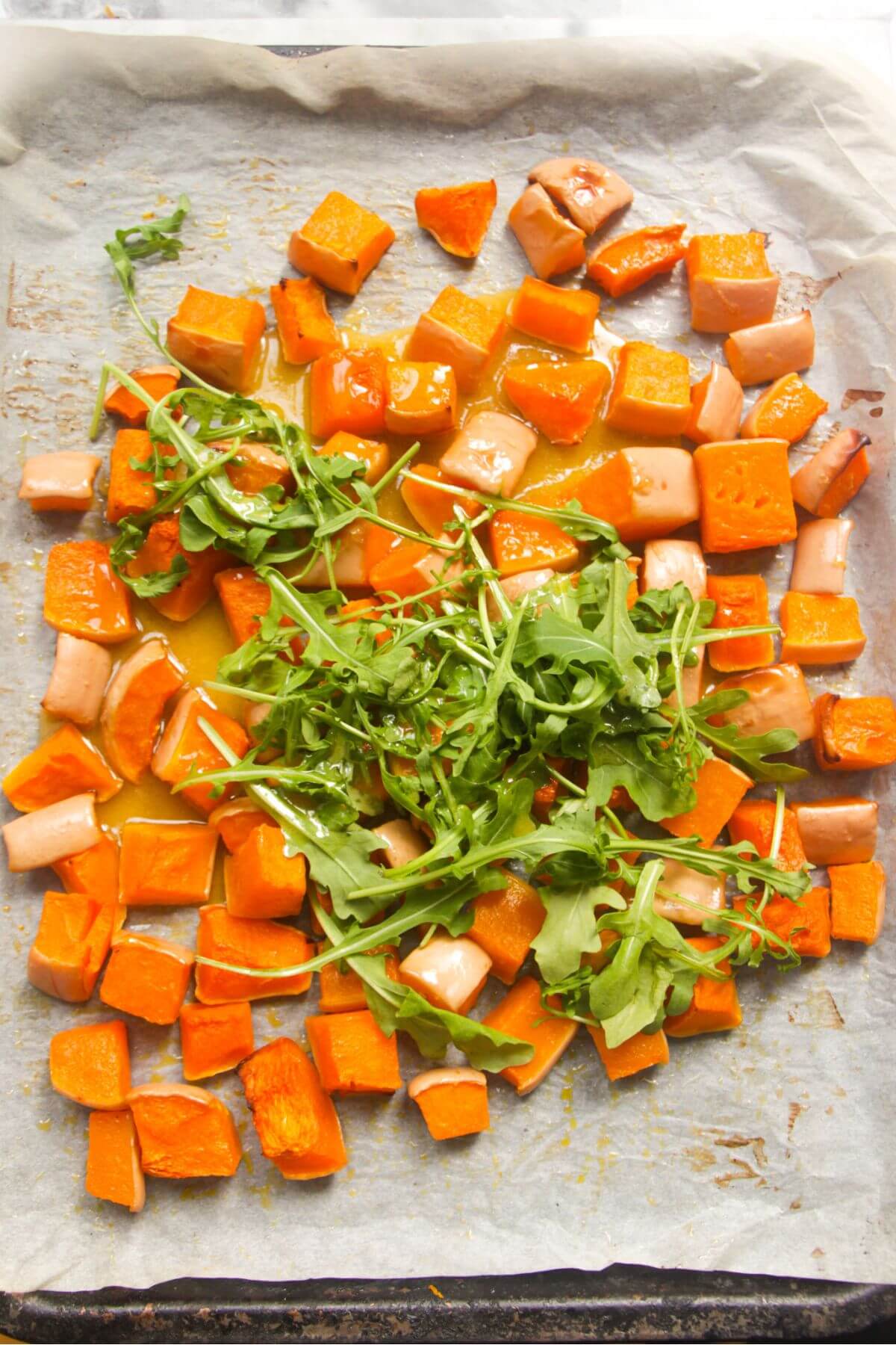 Cooked butternut squash cubes on lined tray with rocket on top.