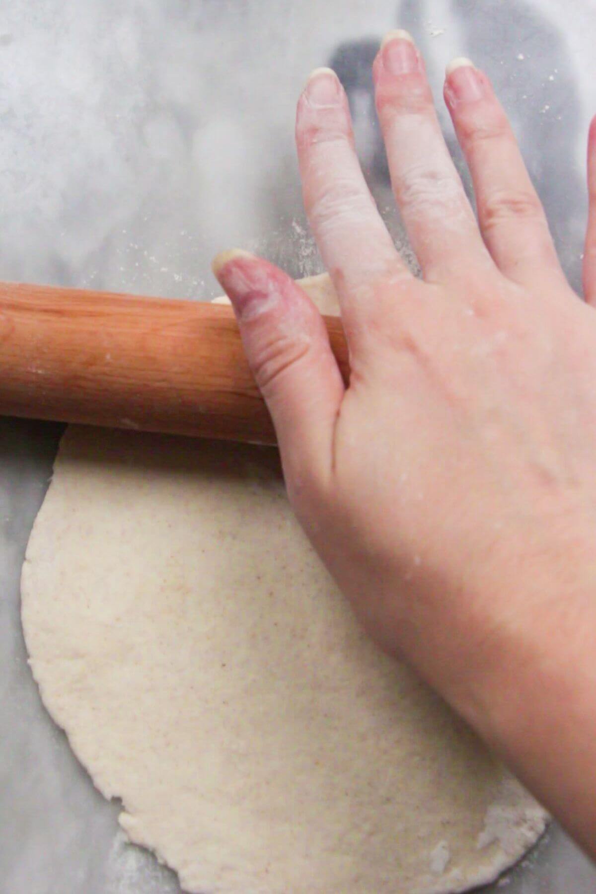 Close up of hand using a wooden rolling pin to roll out garlic naan.