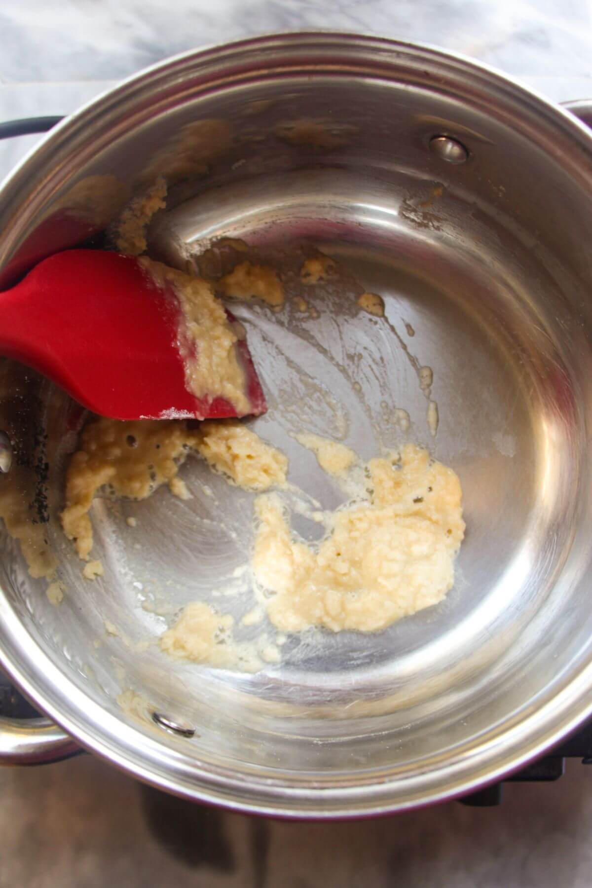 Red spatula stirring butter and flour into a roux in a small silver pot.