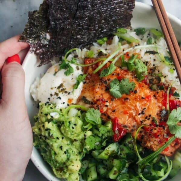 Hand holding a loaded salmon sushi rice bowl.
